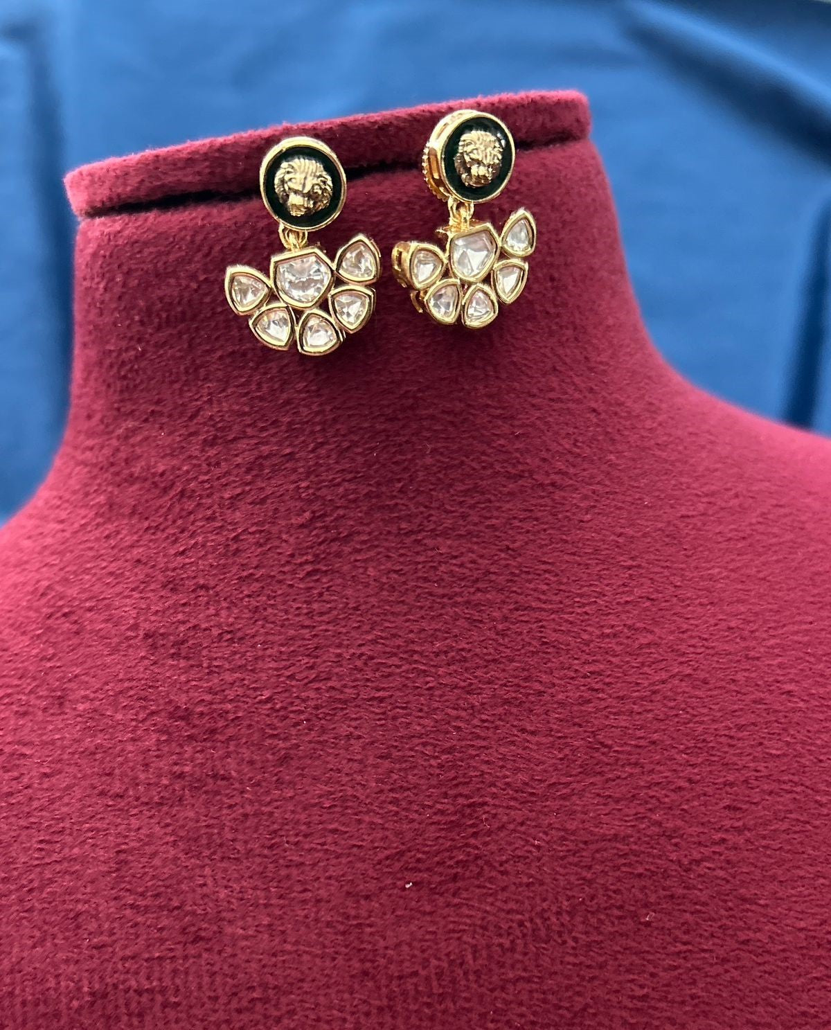 Gold earrings with lion head design on a red mannequin against a blue background