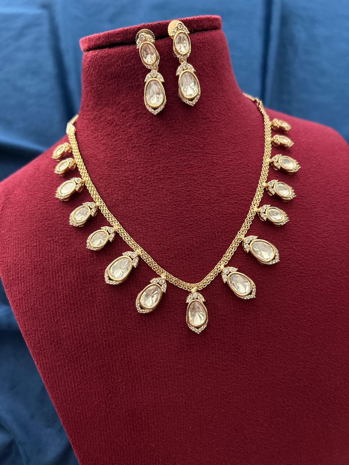 Gold necklace and earrings on a red mannequin against a blue background
