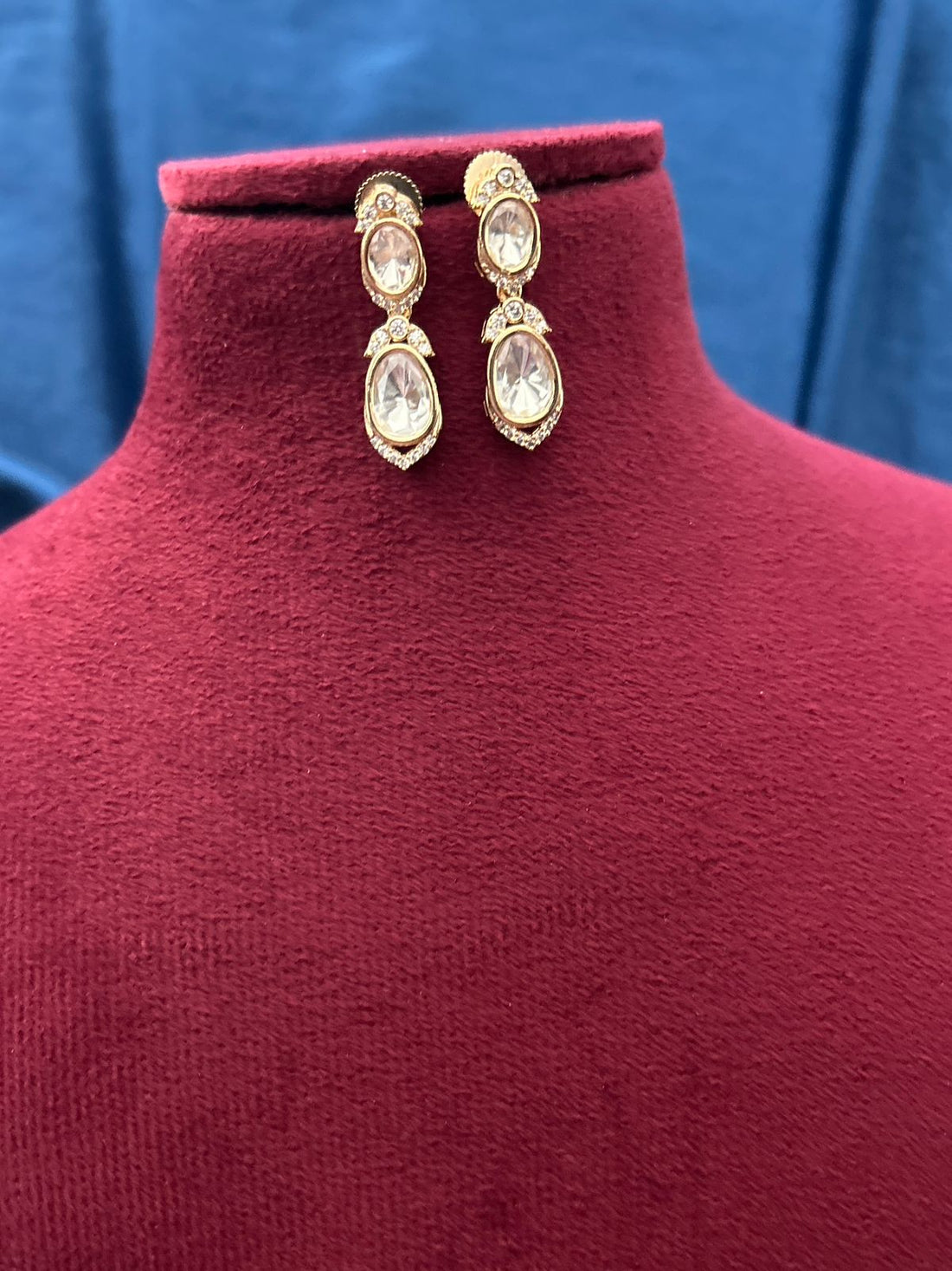Gold earrings with clear stones on a red mannequin against a blue background