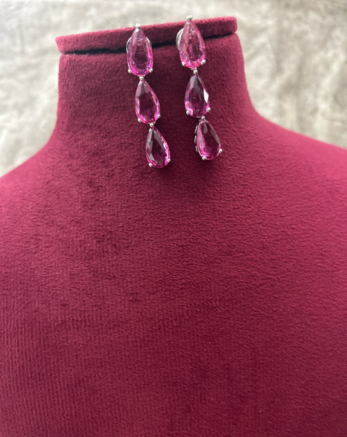 Pink teardrop earrings on a mannequin bust with a textured white background