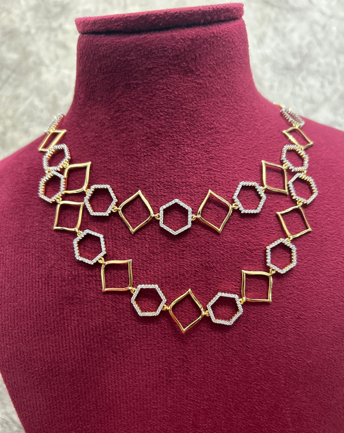 Gold and silver geometric necklace on a mannequin bust with a red background