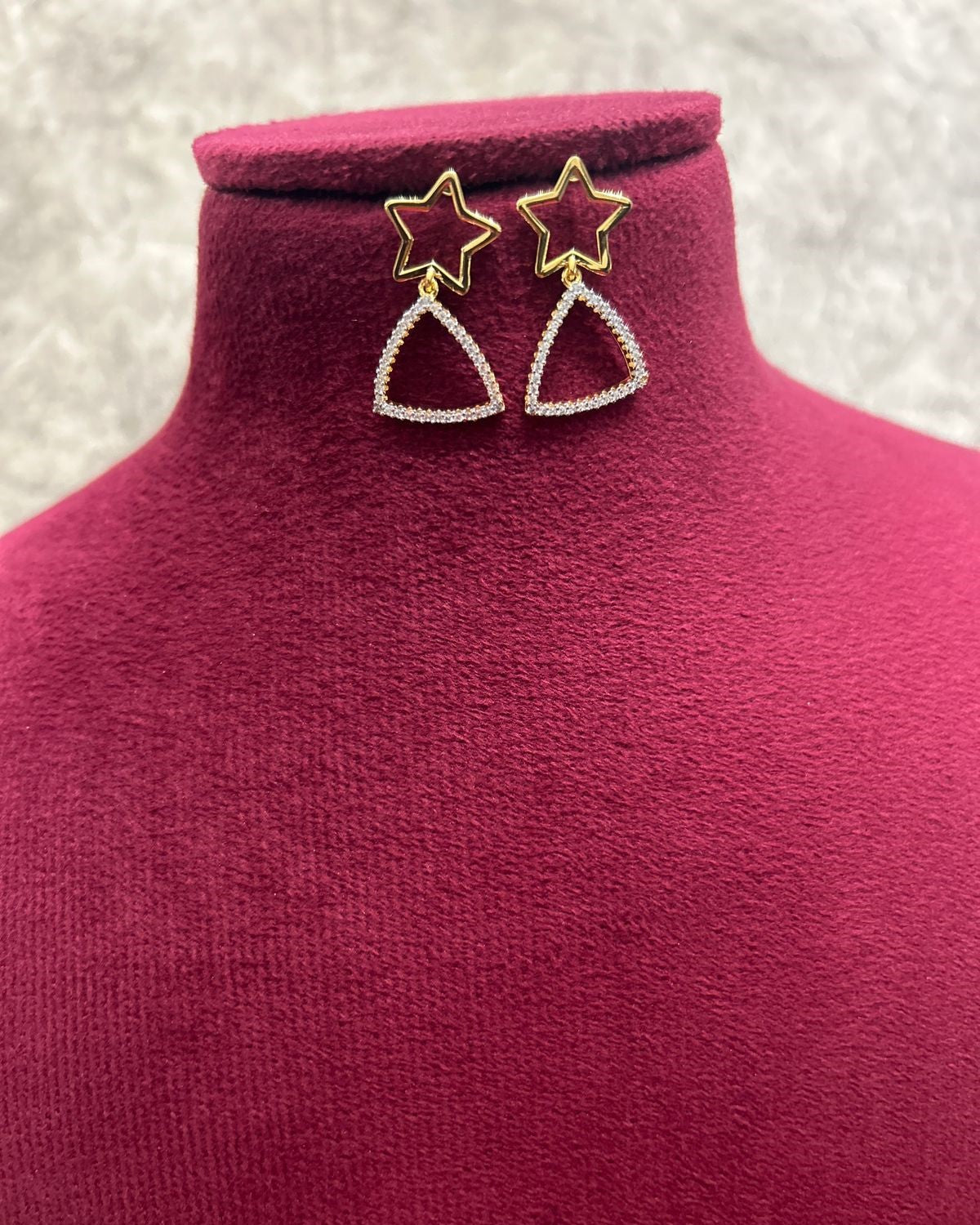 Star-shaped earrings on a pink mannequin with a textured gray background