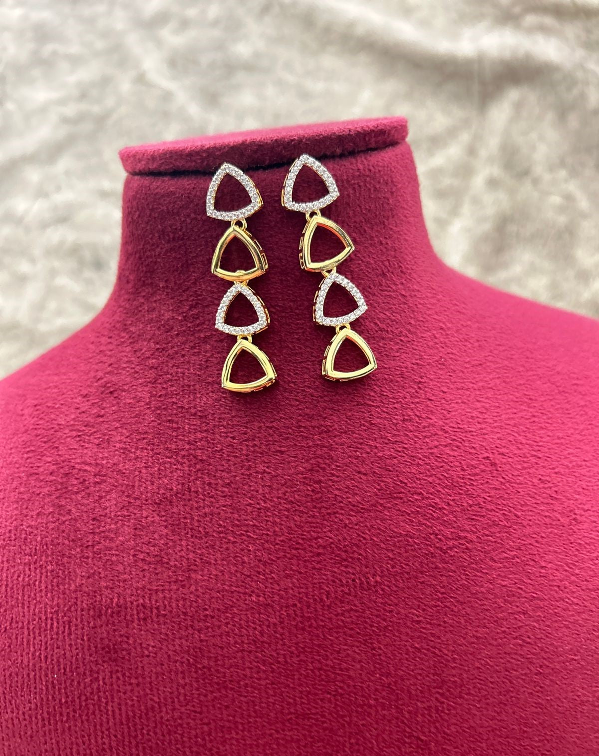 Gold and red earrings on a pink mannequin bust with a neutral background