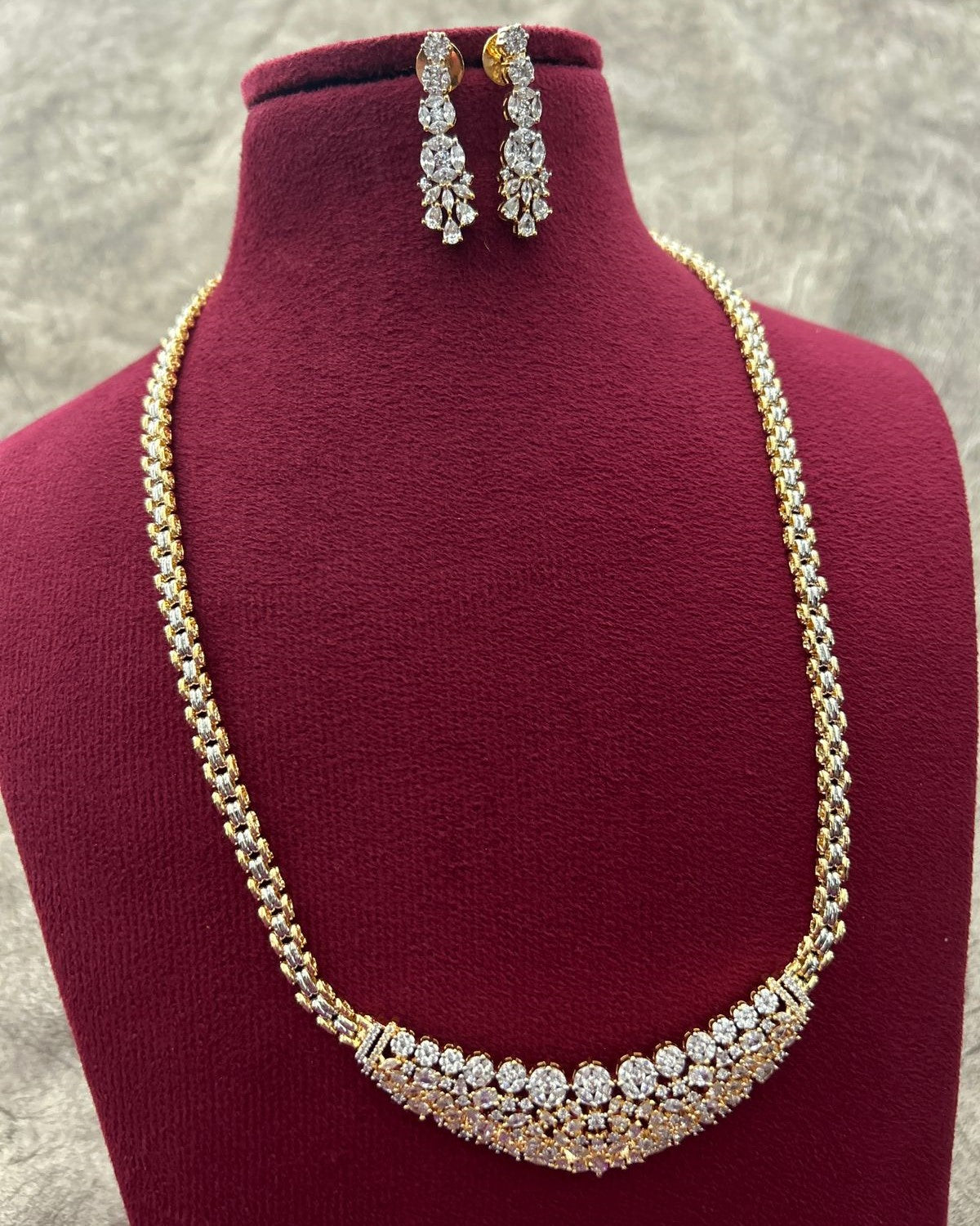 Gold necklace with diamond accents on a red stand, accompanied by matching earrings.
