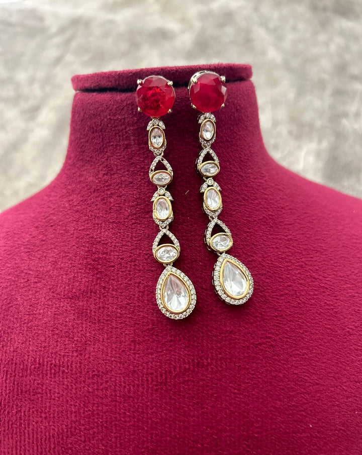 Pair of earrings with red gemstones and teardrop-shaped crystals on a mannequin bust.