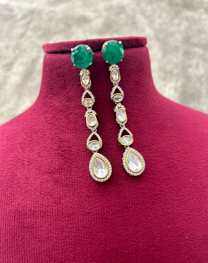Pair of earrings with green gemstones and teardrop designs on a mannequin bust.
