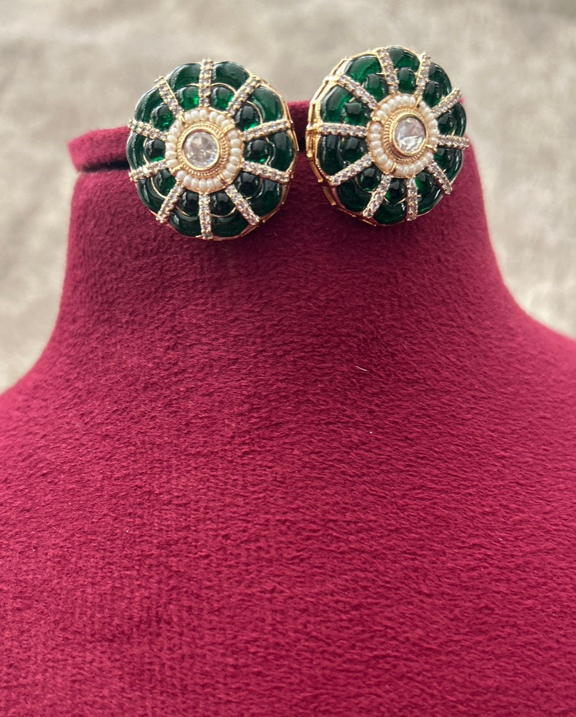 Green and gold earrings on a mannequin bust with a textured background