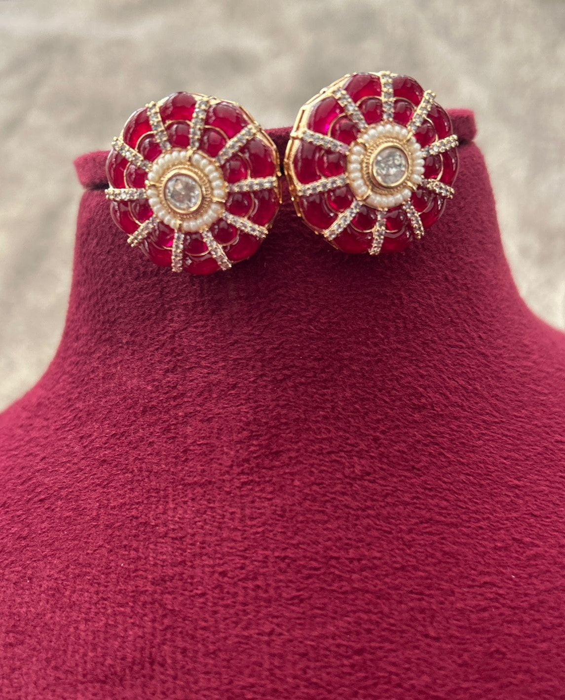 Pair of red and gold earrings on a pink stand with a blurred background