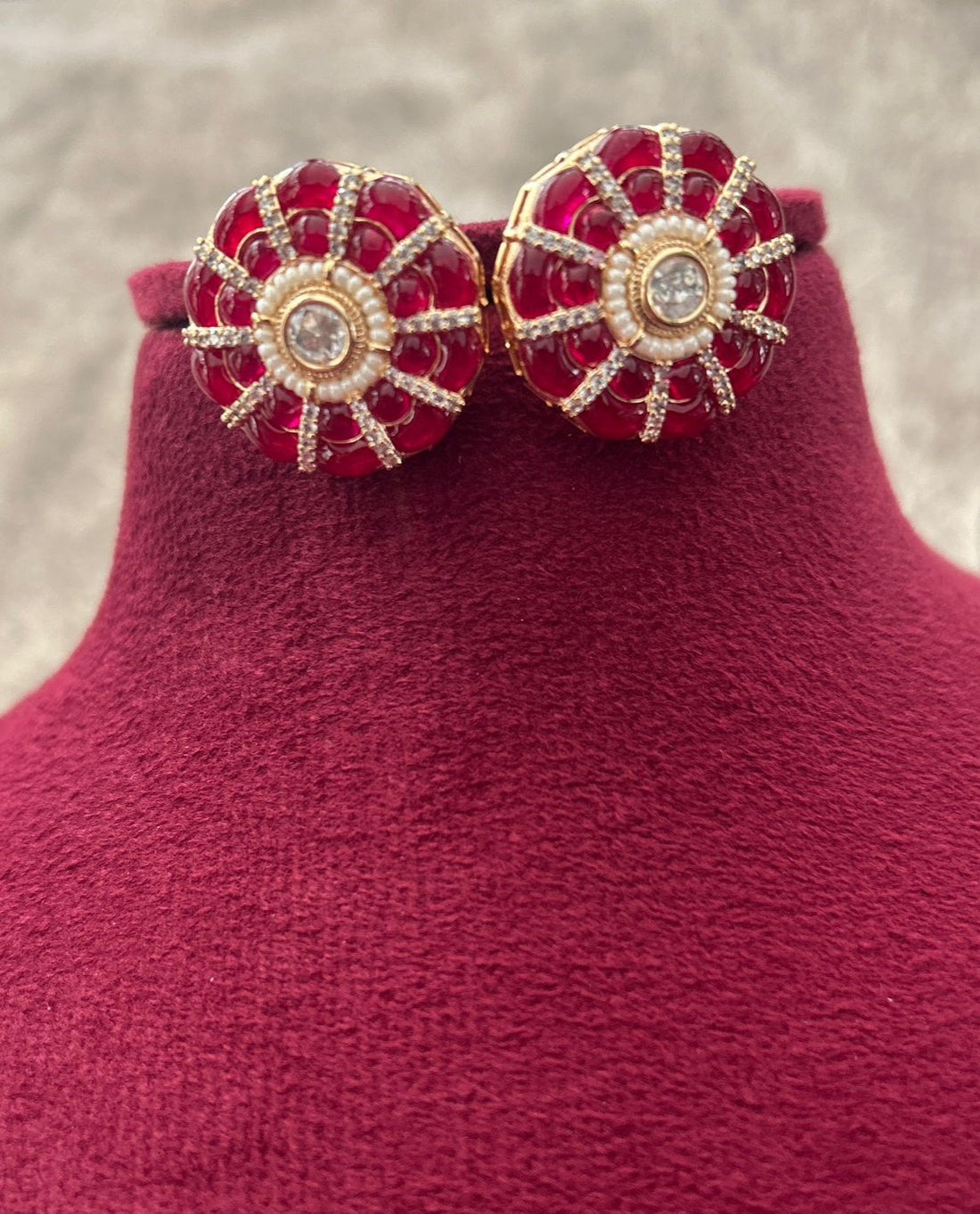 Pair of red and gold earrings on a pink stand with a blurred background