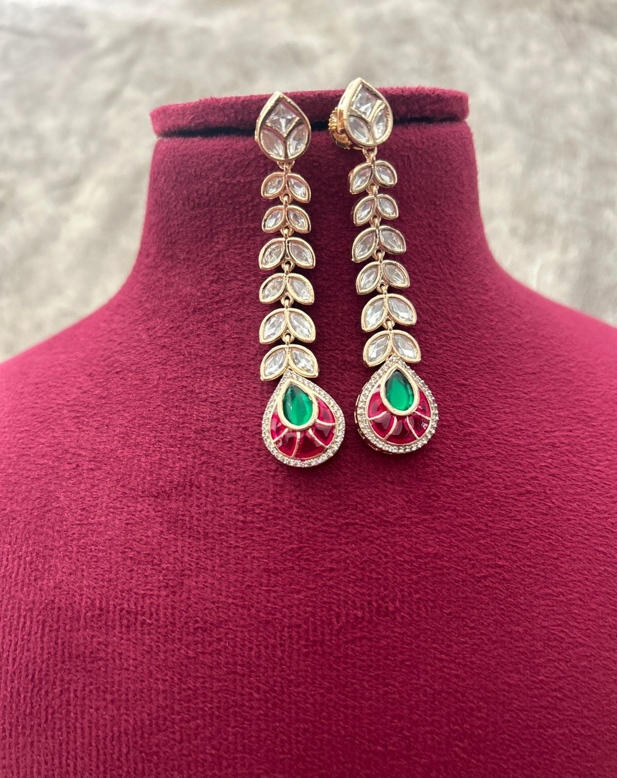 Ornate earrings with green and red stones on a mannequin bust.