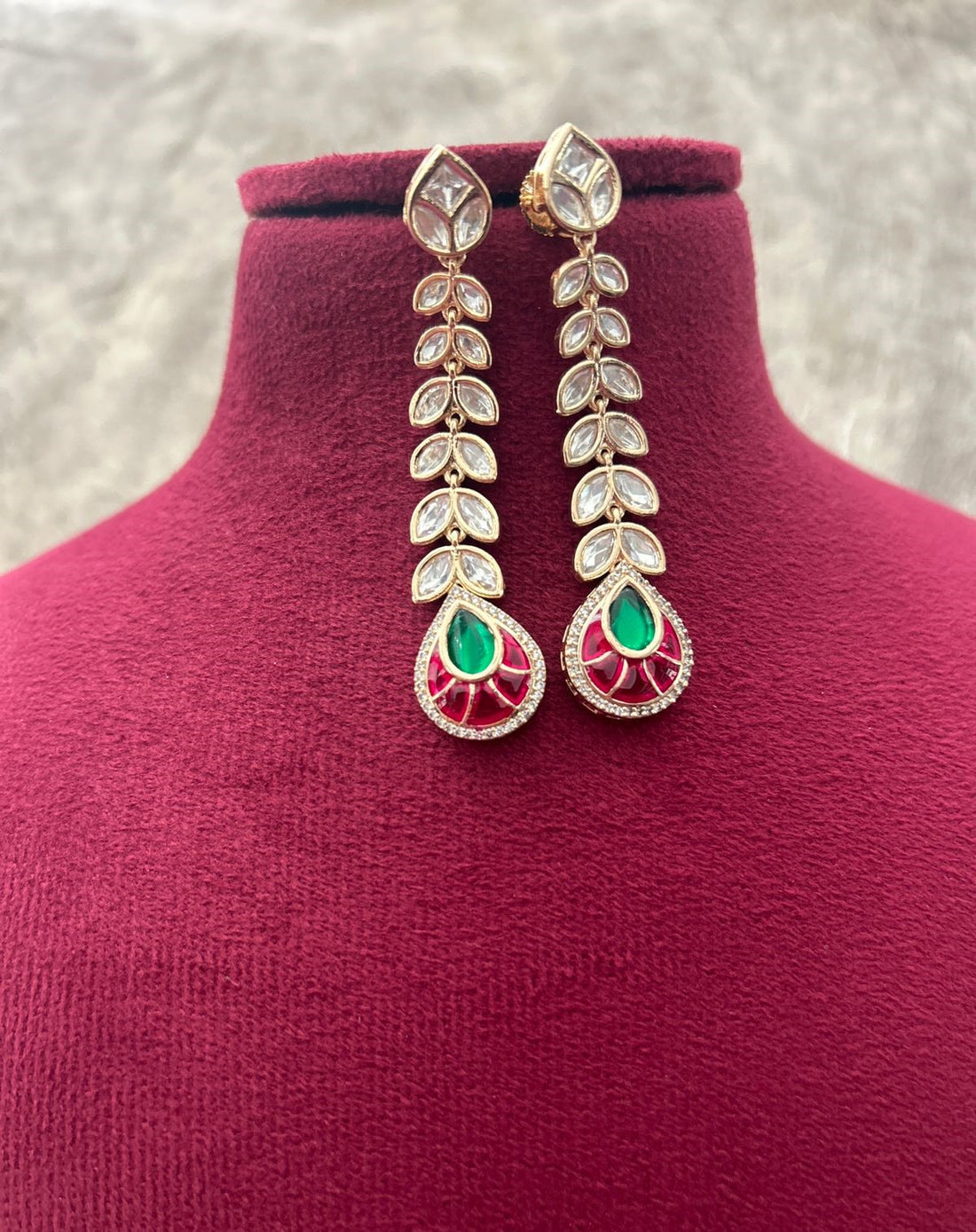 Ornate earrings with green and red stones on a mannequin bust.