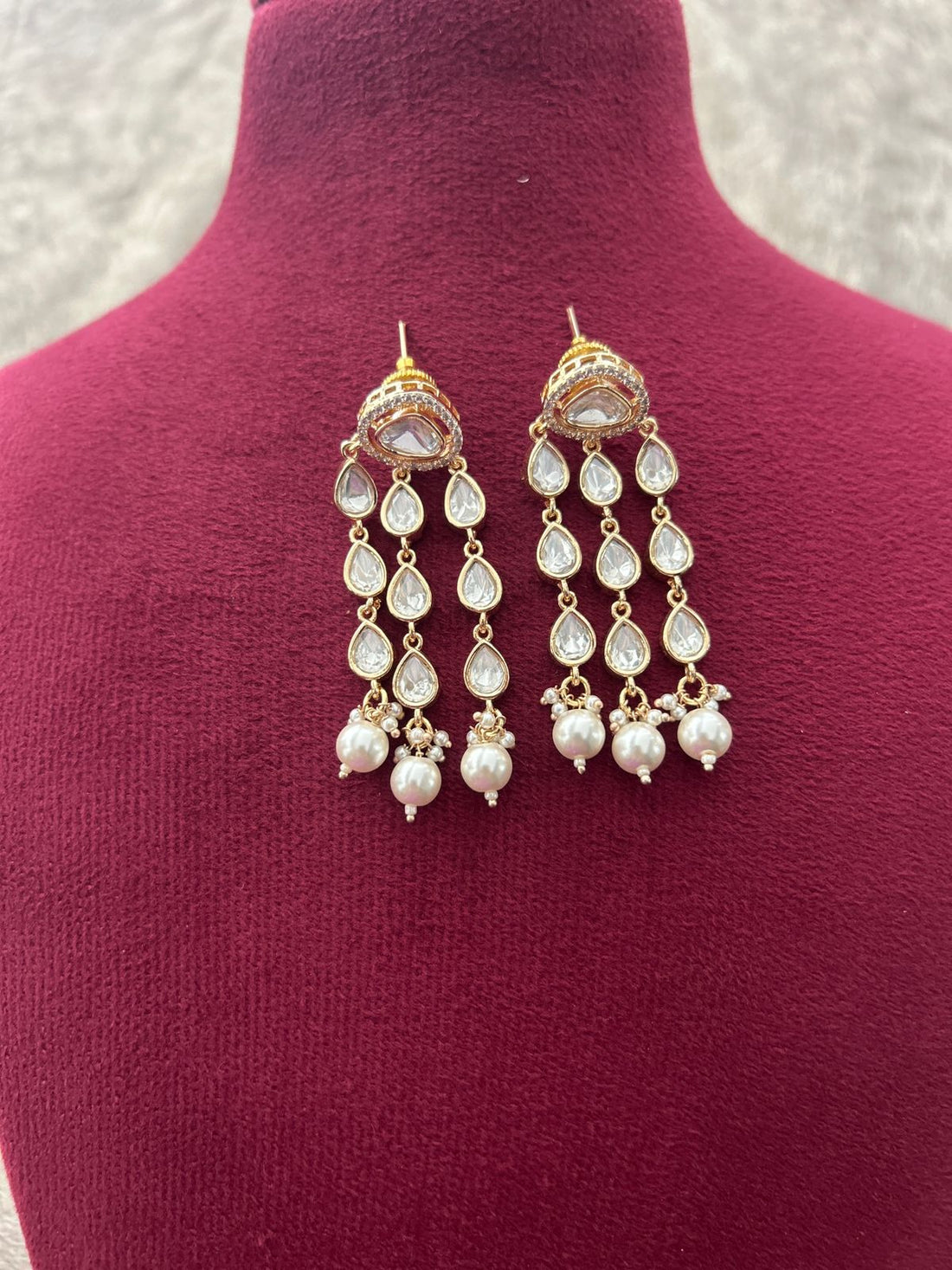 Pair of gold and pearl earrings on a mannequin with a textured background