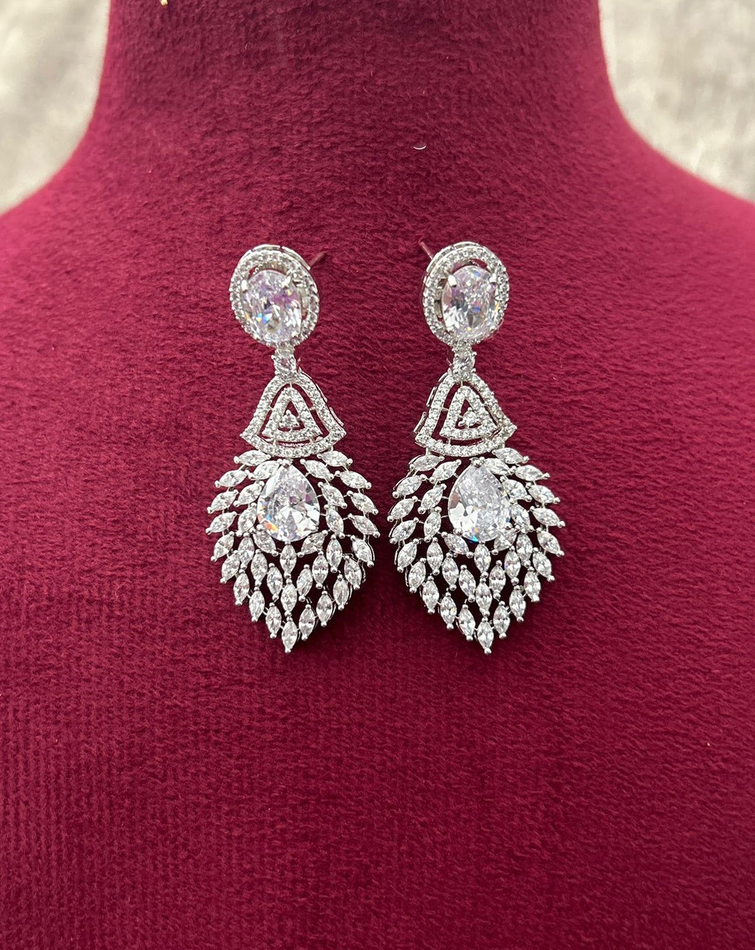 Pair of silver earrings with clear stones on a red fabric background