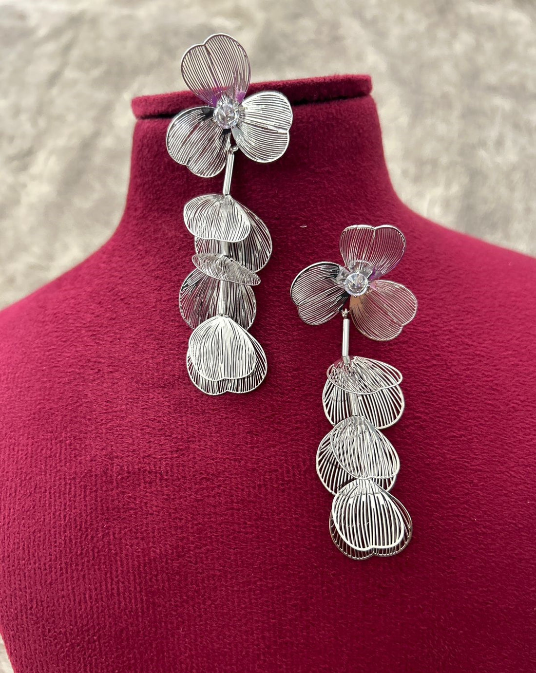 Silver floral earrings on a red velvet stand with a neutral background