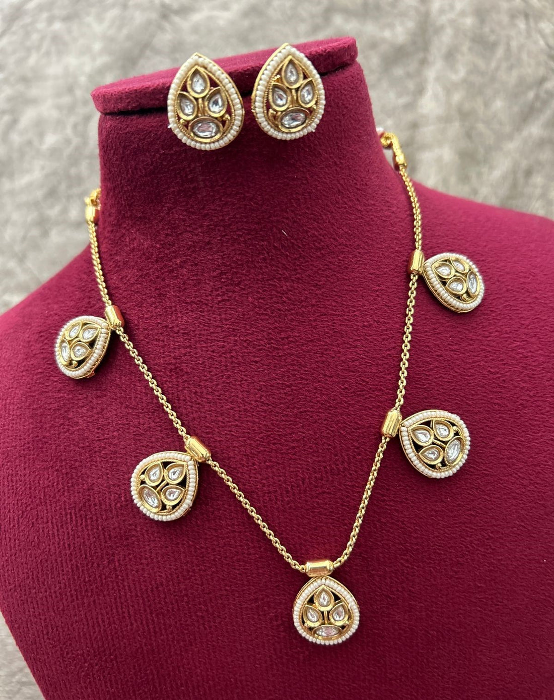 Gold necklace and earrings set on a mannequin bust with a gray background