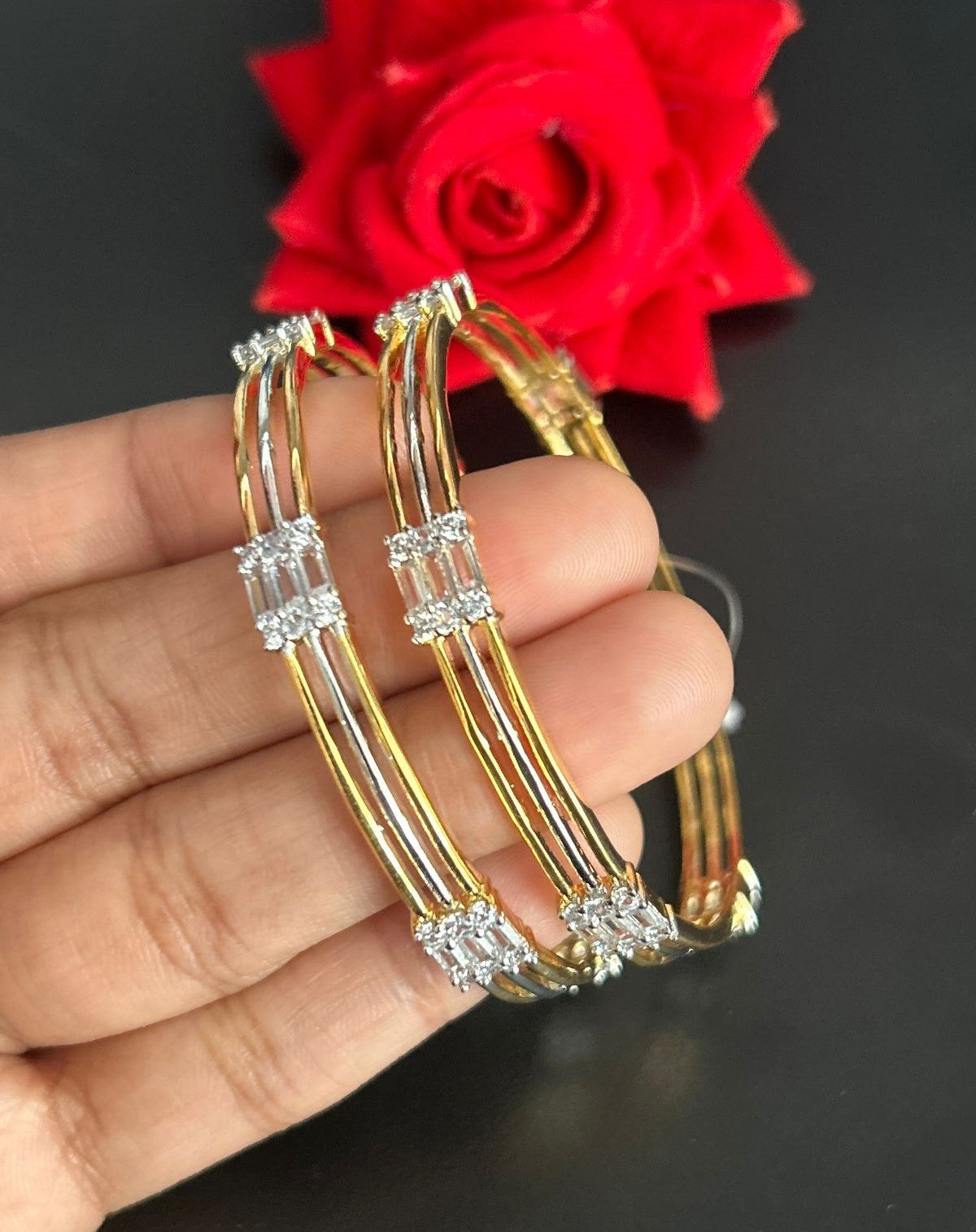 Gold hoop earrings with diamonds held by a hand against a red rose background