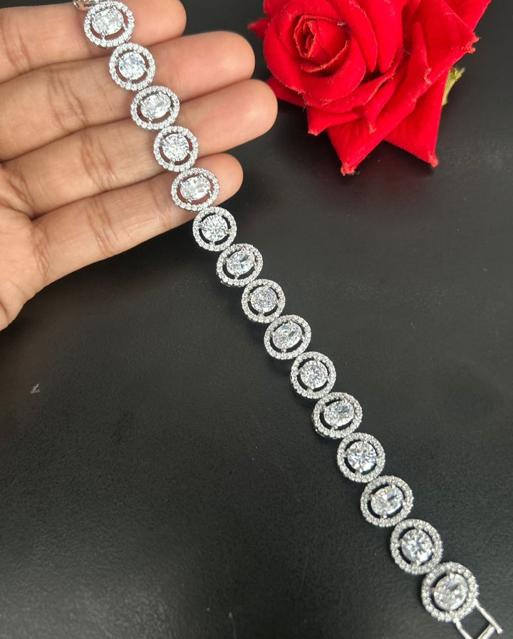 Silver bracelet with circular design held by a hand on a black surface with a red rose in the background.