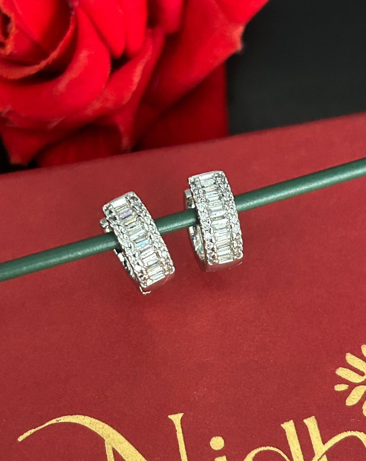 Silver hoop earrings on a green stick with a red rose and box in the background