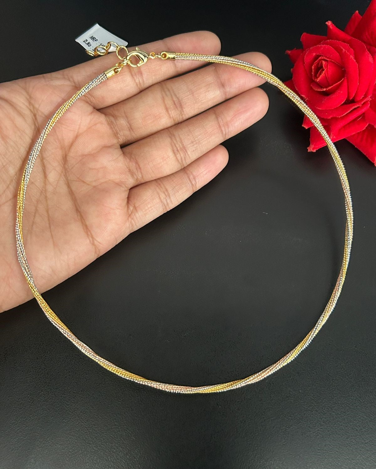 Gold necklace being held by a hand with a red rose in the background
