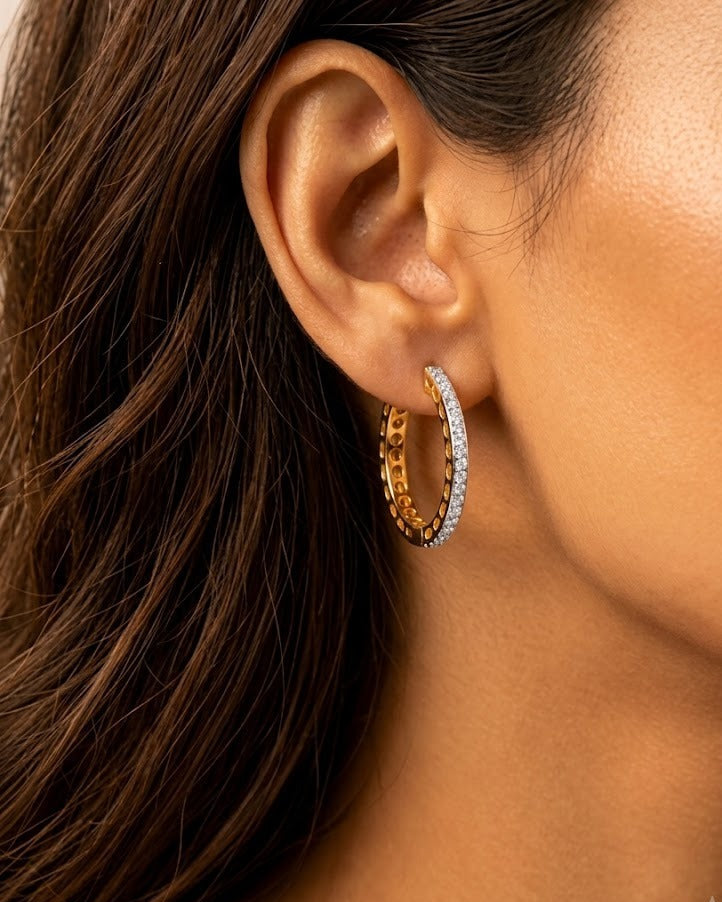 Close-up of a person wearing gold hoop earrings with a blurred background