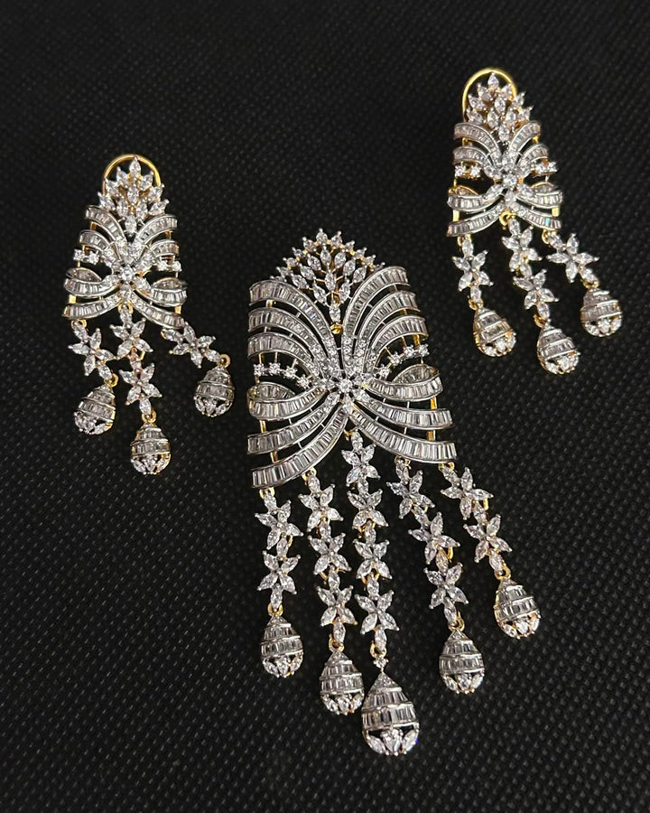 A three-piece traditional Indian jewelry set featuring a large central choker and two matching dangling earrings, all adorned with silver-toned metal and clear stones, displayed on a textured black background.