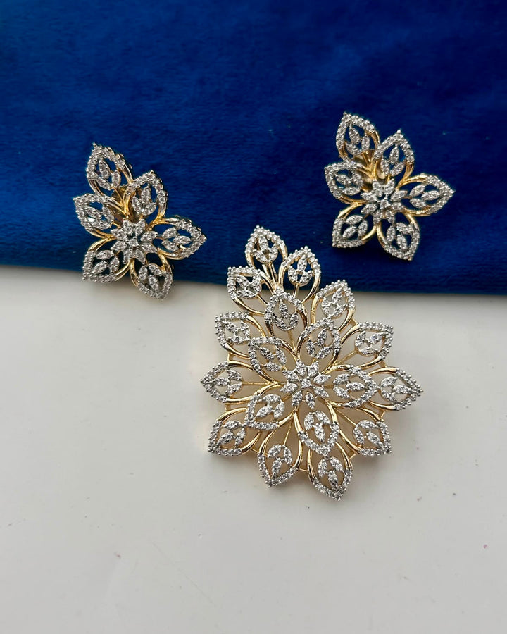 A pair of gold and silver floral stud earrings with clear pavé stones, displayed on a split white and dark blue velvet background.