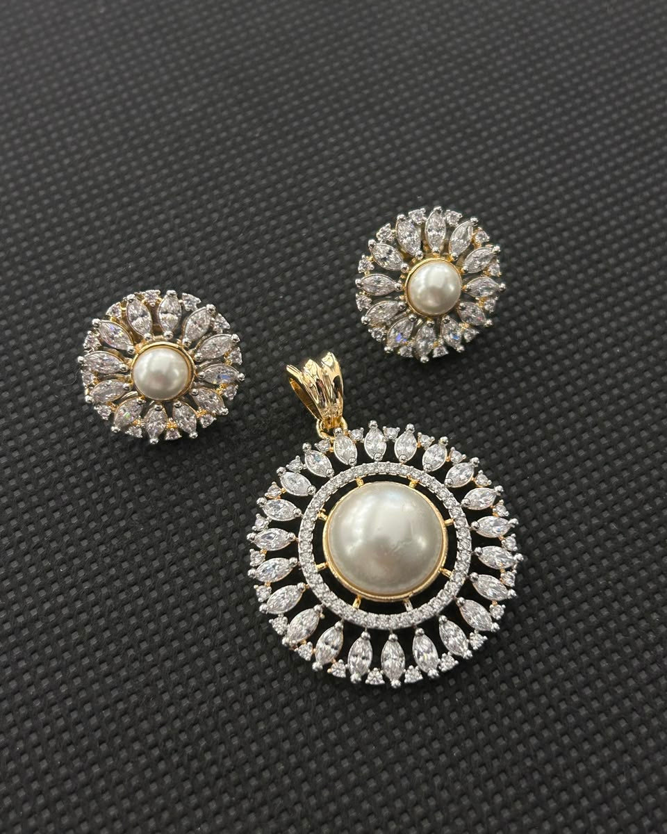 A gold and white pearl jewelry set featuring a large pendant and matching stud earrings, both adorned with clear crystals, displayed on a textured black background.