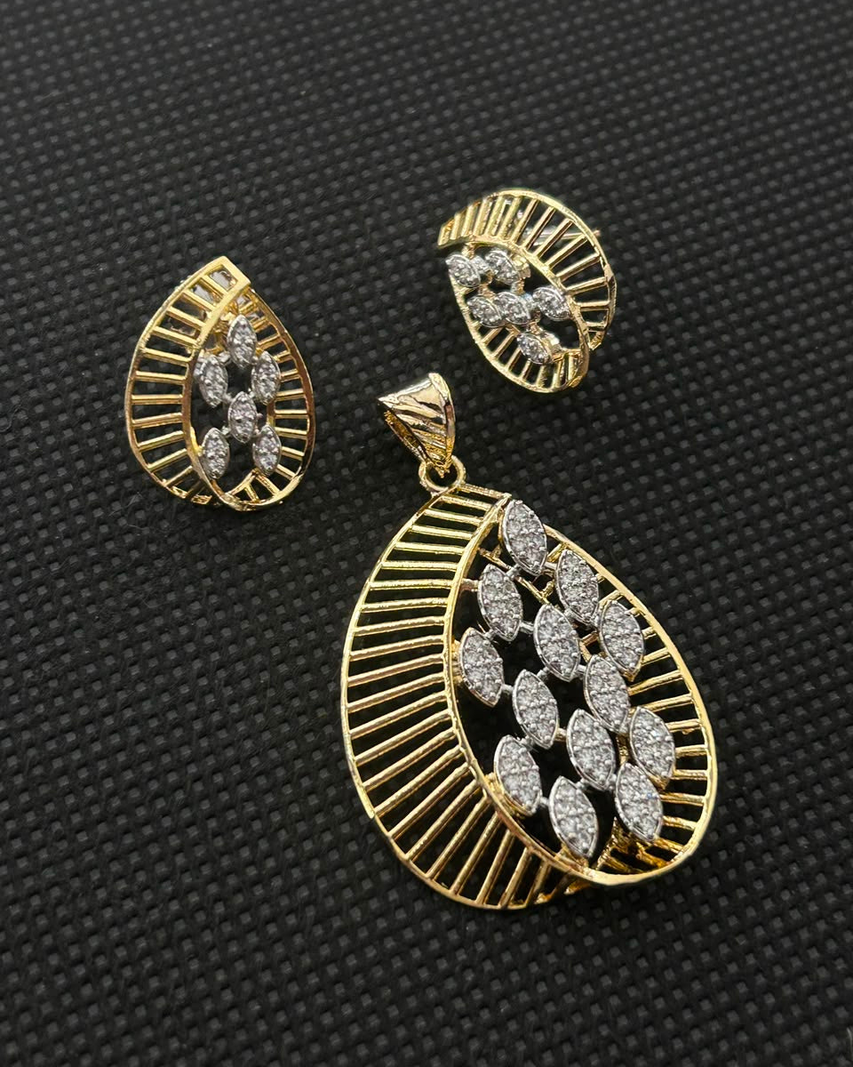 Gold-toned statement earrings and matching pendant set with pavé-set clear stones, displayed on a textured black background.