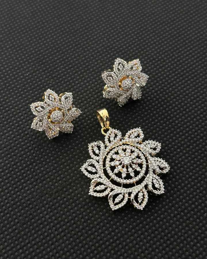 A pair of silver-toned flower-shaped stud earrings and a matching large pendant with intricate pavé detailing, displayed on a textured black background.