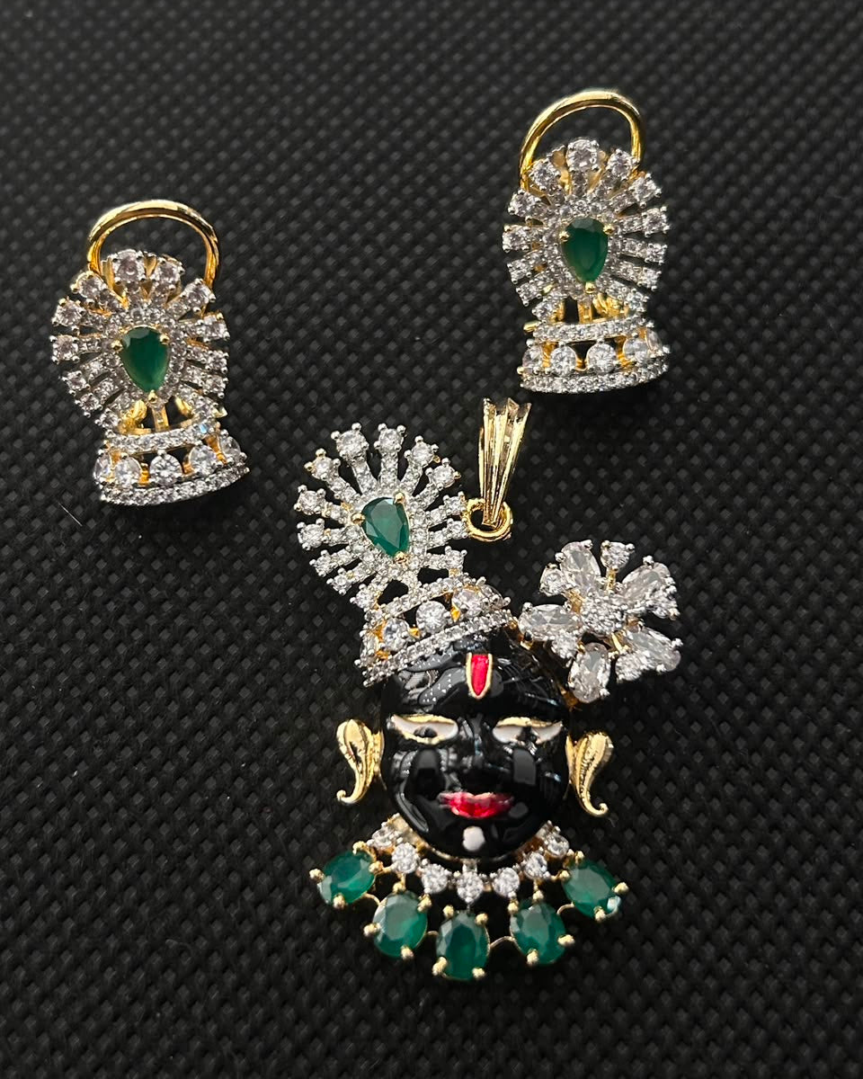 Gold and silver jewelry set featuring a black and red deity pendant with green stones, accompanied by matching earrings, displayed on a black textured background.