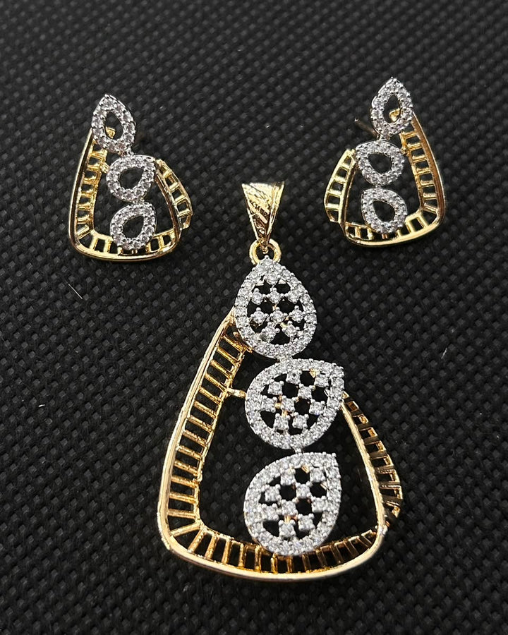 Gold and silver-tone jewelry set featuring a teardrop-shaped pendant and matching earrings, embellished with clear stones on a textured black background.