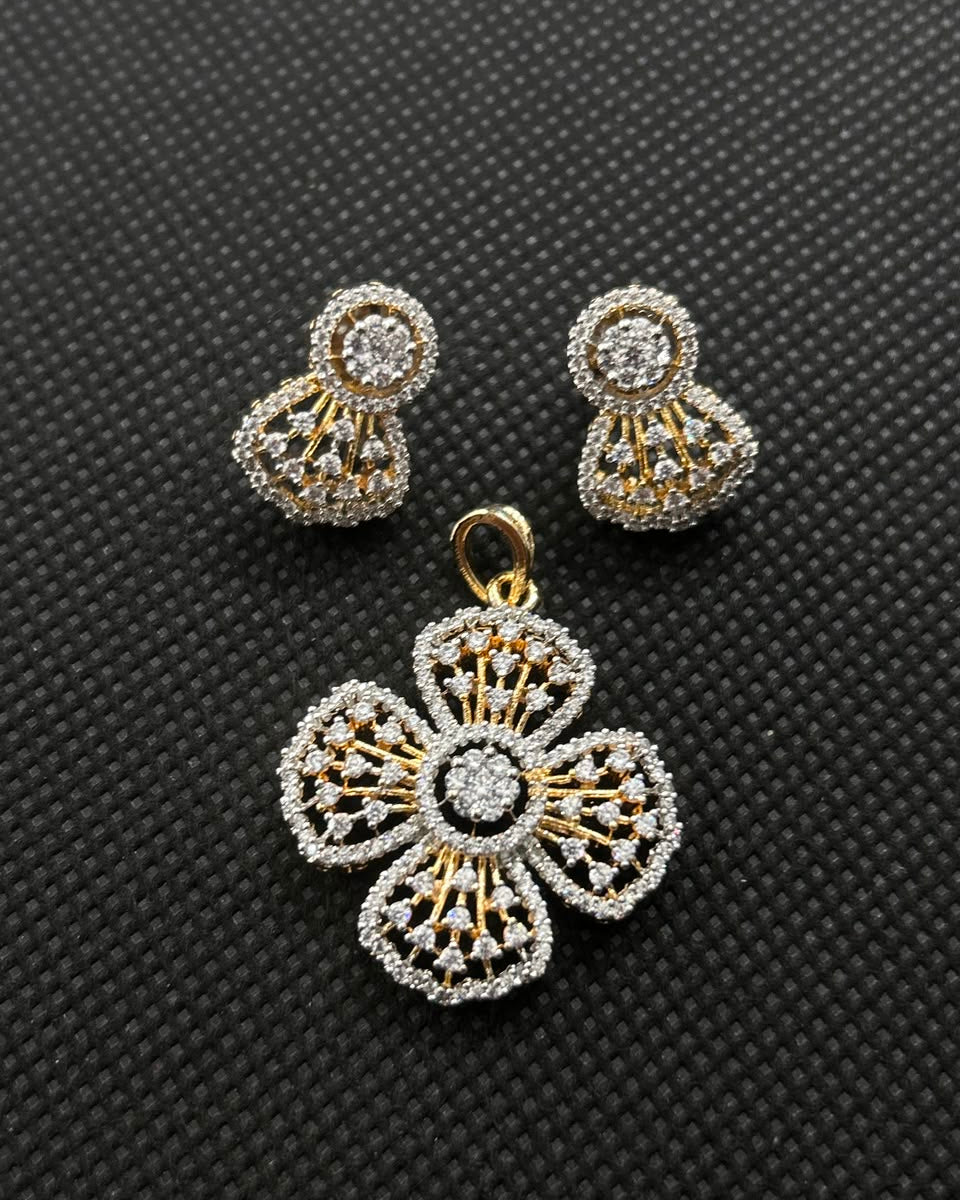 A gold and silver-toned jewelry set featuring a floral pendant and matching stud earrings, displayed on a textured black background.