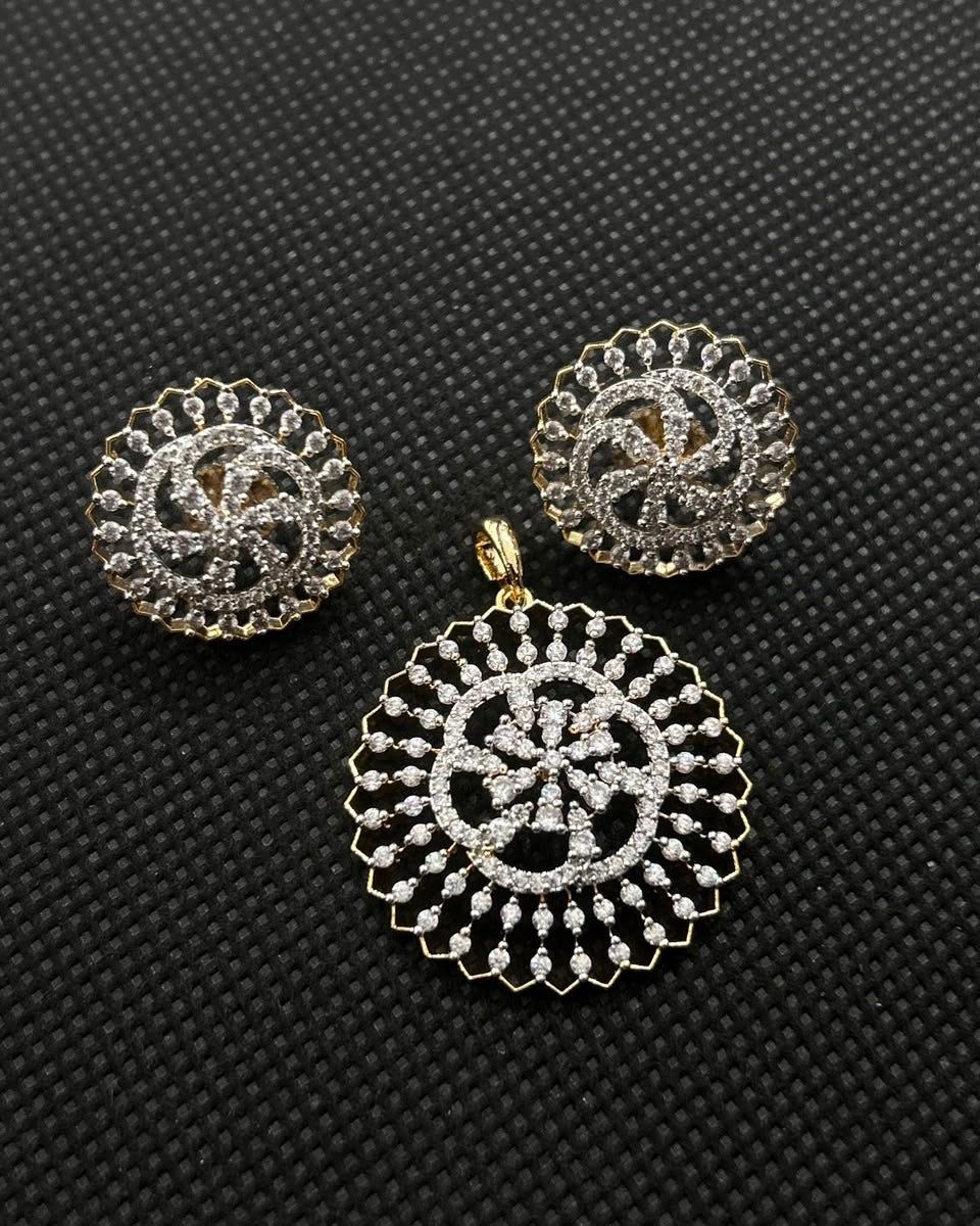 A pair of gold and silver-toned earrings with a matching circular pendant, featuring intricate filigree cutout patterns, displayed on a textured black background.