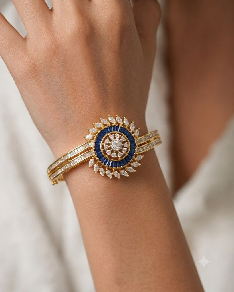 A close-up of a gold bangle bracelet with a central blue and white circular motif, adorned with small clear stones, worn on a person's wrist.