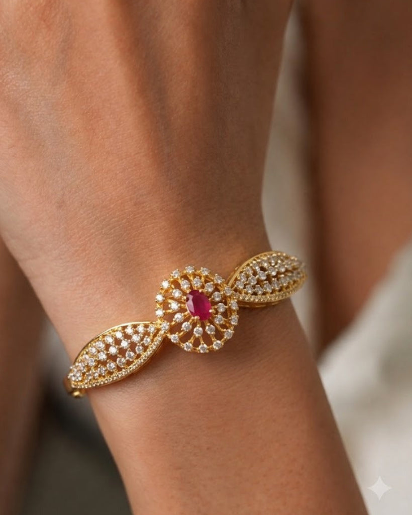 A close-up of a gold-toned bracelet with a central oval pink gemstone surrounded by small clear stones, worn on a person's wrist.