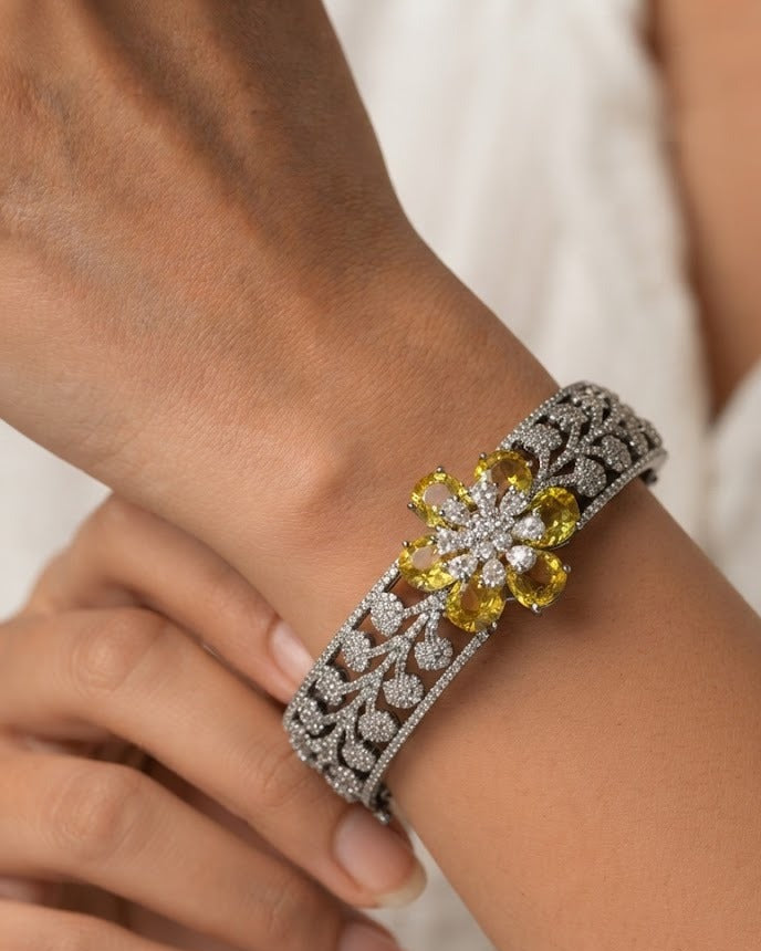 A close-up of a silver-toned filigree cuff bracelet with a yellow gemstone flower centerpiece, worn on a person's wrist.