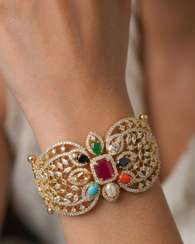A close-up of a gold-toned filigree cuff bracelet with multiple colorful gemstones, worn on a person's wrist.