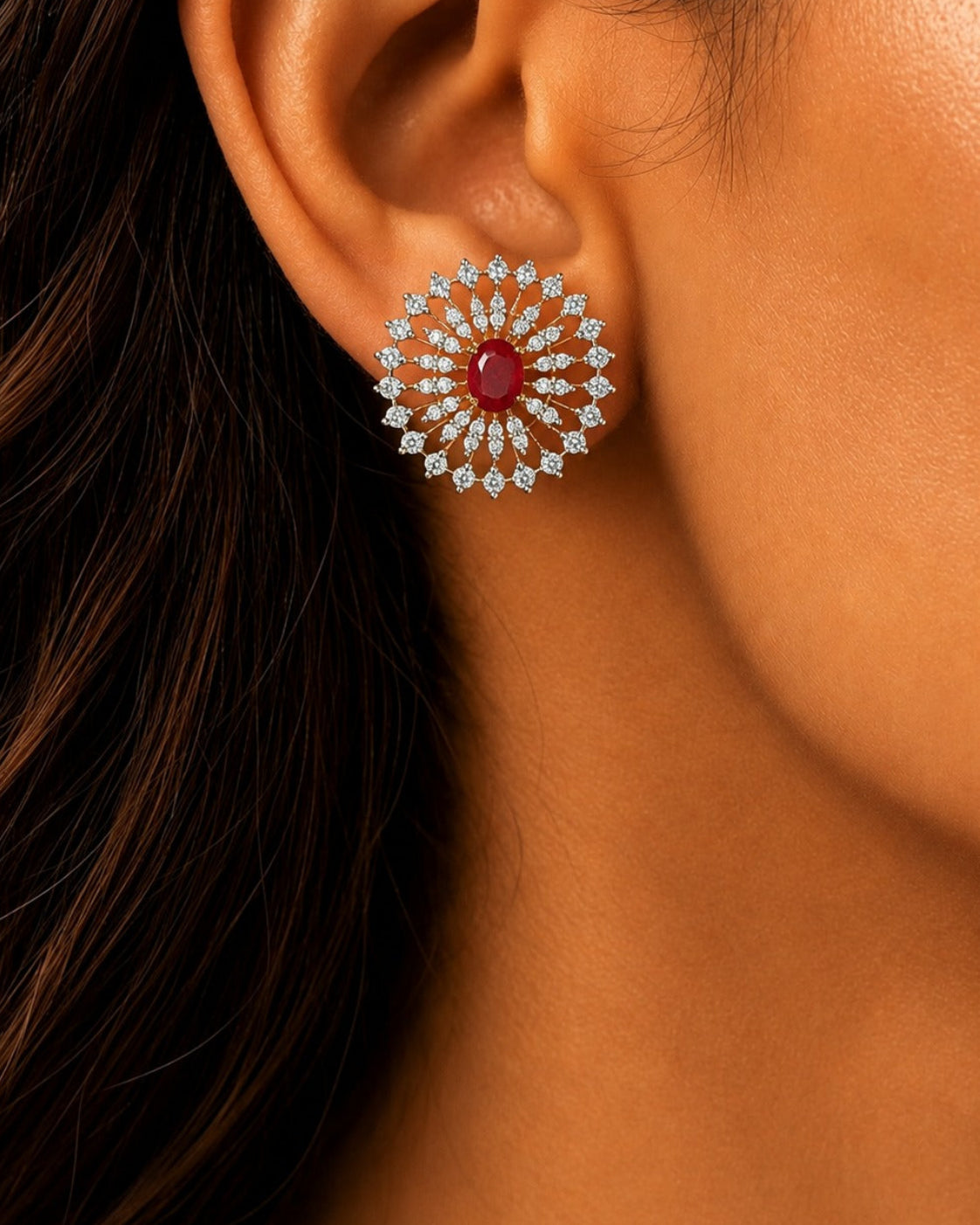 A close-up of a woman's ear wearing a circular silver-toned earring with a central red gemstone surrounded by small clear stones.