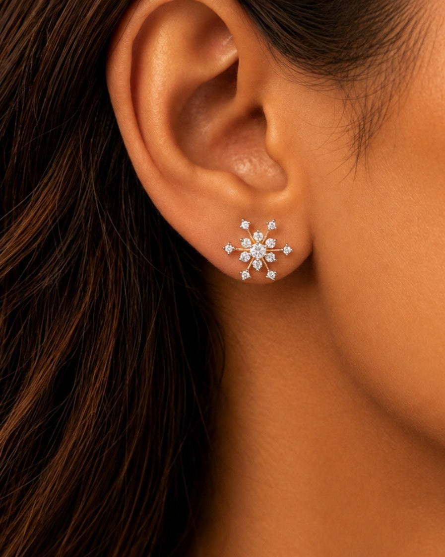 A close-up of a person's ear wearing a small snowflake-shaped stud earring with clear stones in a silver-toned setting.