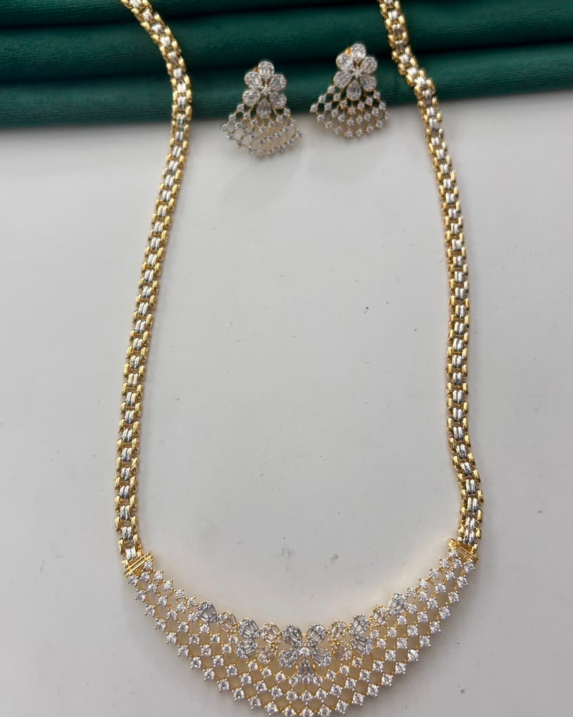 Gold-plated chain necklace and matching stud earrings set with clear rhinestones, displayed on a white surface with a dark green fabric backdrop.