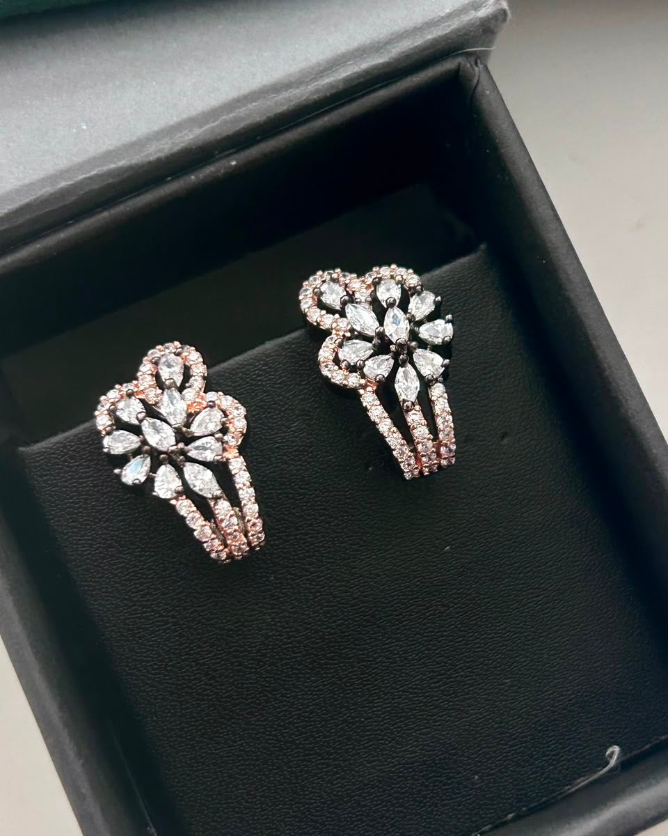 A pair of rose gold floral stud earrings with clear marquise and round-cut stones, displayed on a black velvet jewelry cushion inside an open black presentation box.