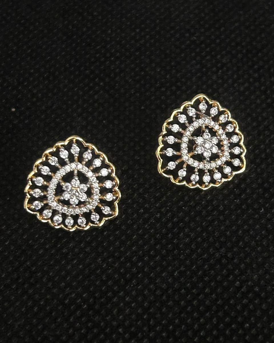 A pair of gold-toned stud earrings with intricate silver-toned pavé detailing, displayed on a textured black background.