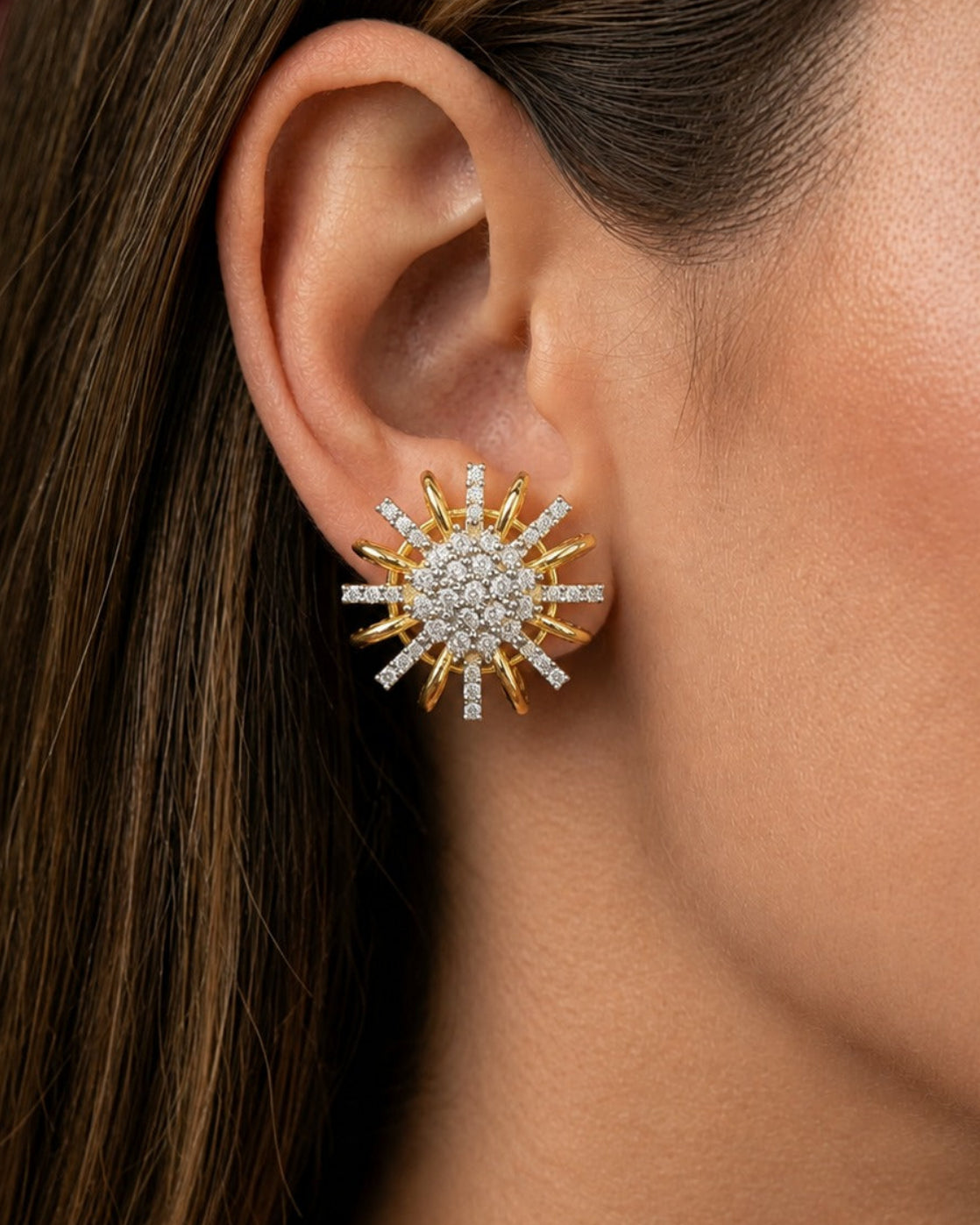 A close-up of a model's ear wearing a gold and white stone sunburst stud earring.