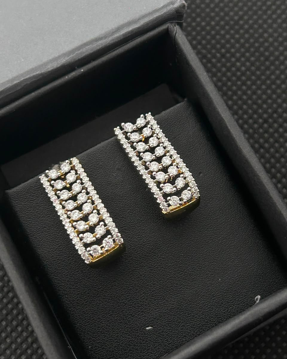 A pair of gold and silver-tone rectangular stud earrings with rows of clear stones, displayed inside an open black jewelry box.