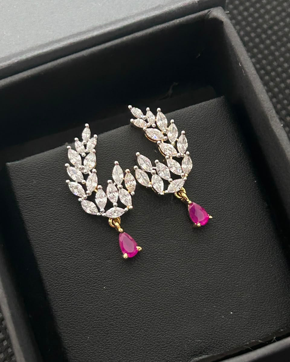 A pair of gold and silver leaf-shaped drop earrings with clear marquise-cut stones and pink teardrop gemstones, displayed on a black jewelry box.