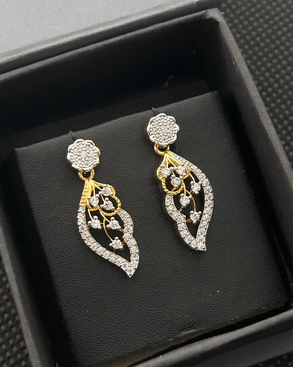 A pair of gold and silver drop earrings with pavé-set clear stones, displayed on a black velvet cushion inside a black gift box.