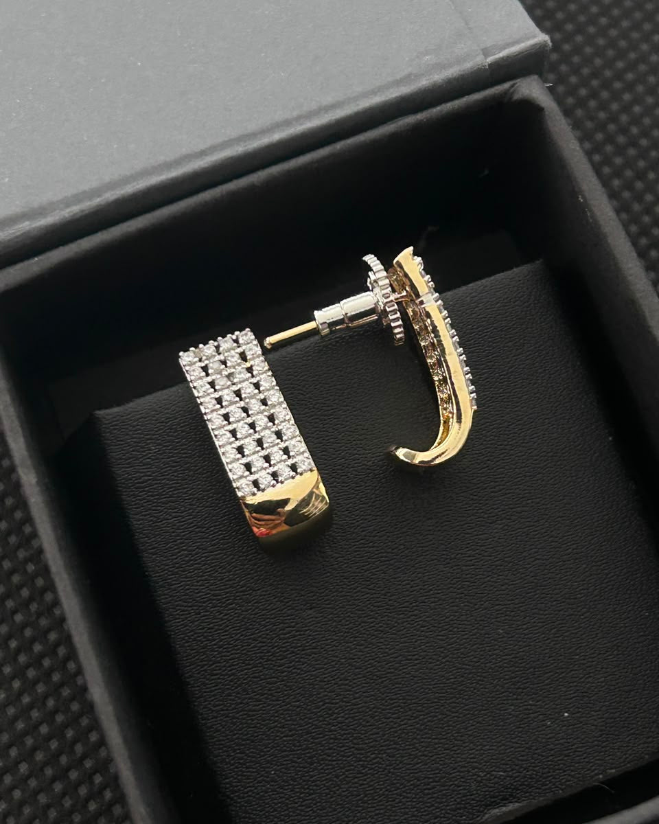 A pair of gold and silver-tone huggie hoop earrings with clear crystal embellishments, displayed inside a black presentation box.