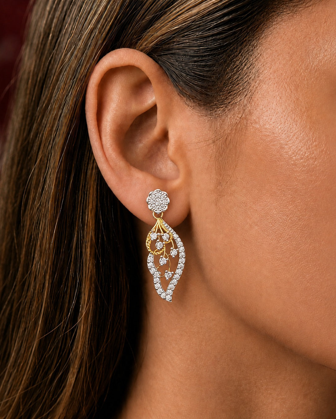 A close-up of a woman's ear wearing a gold and white stone drop earring with a floral stud and an ornate teardrop-shaped dangling design.