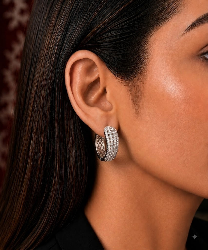 A close-up side profile of a woman wearing a silver hoop earring adorned with rows of small clear stones and a textured inner band.