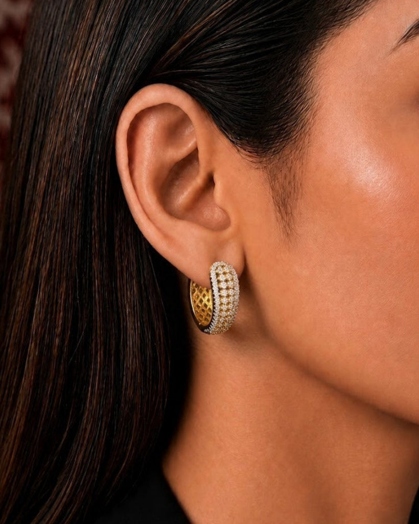 A close-up side profile of a woman wearing a gold and white pave-studded hoop earring.